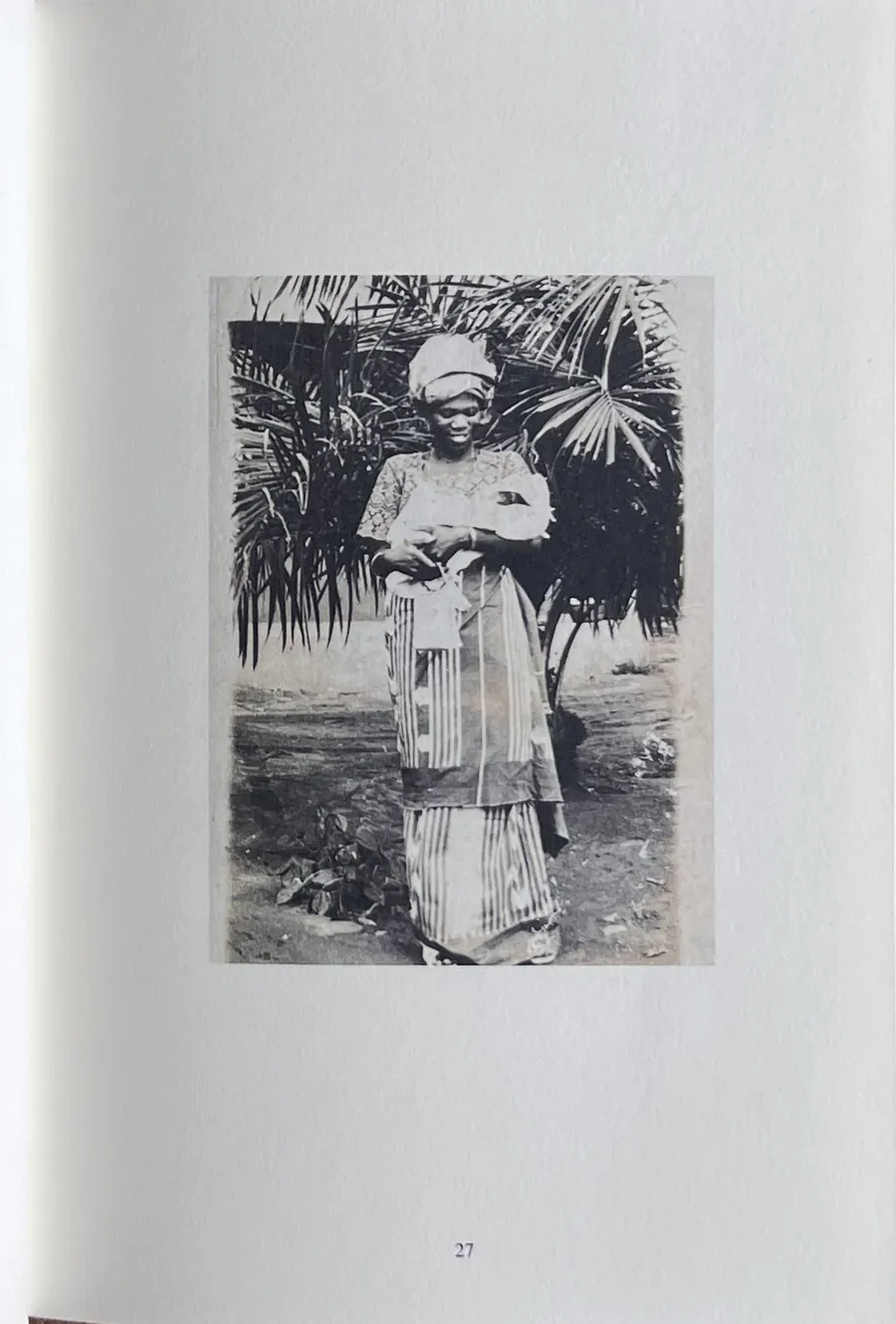 Page 27 of the printed book, photographed: a restored family photograph of a woman in patterned cloth before palm fronds, printed on cream paper.