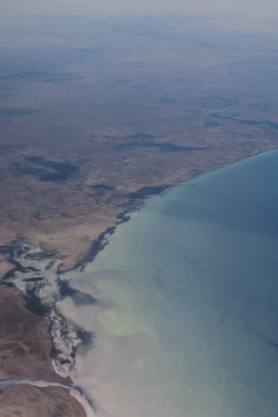 An aerial photograph across two pages: a river delta spills pale water into the sea along a curving coast, which runs on into deep blue water on the facing page.
